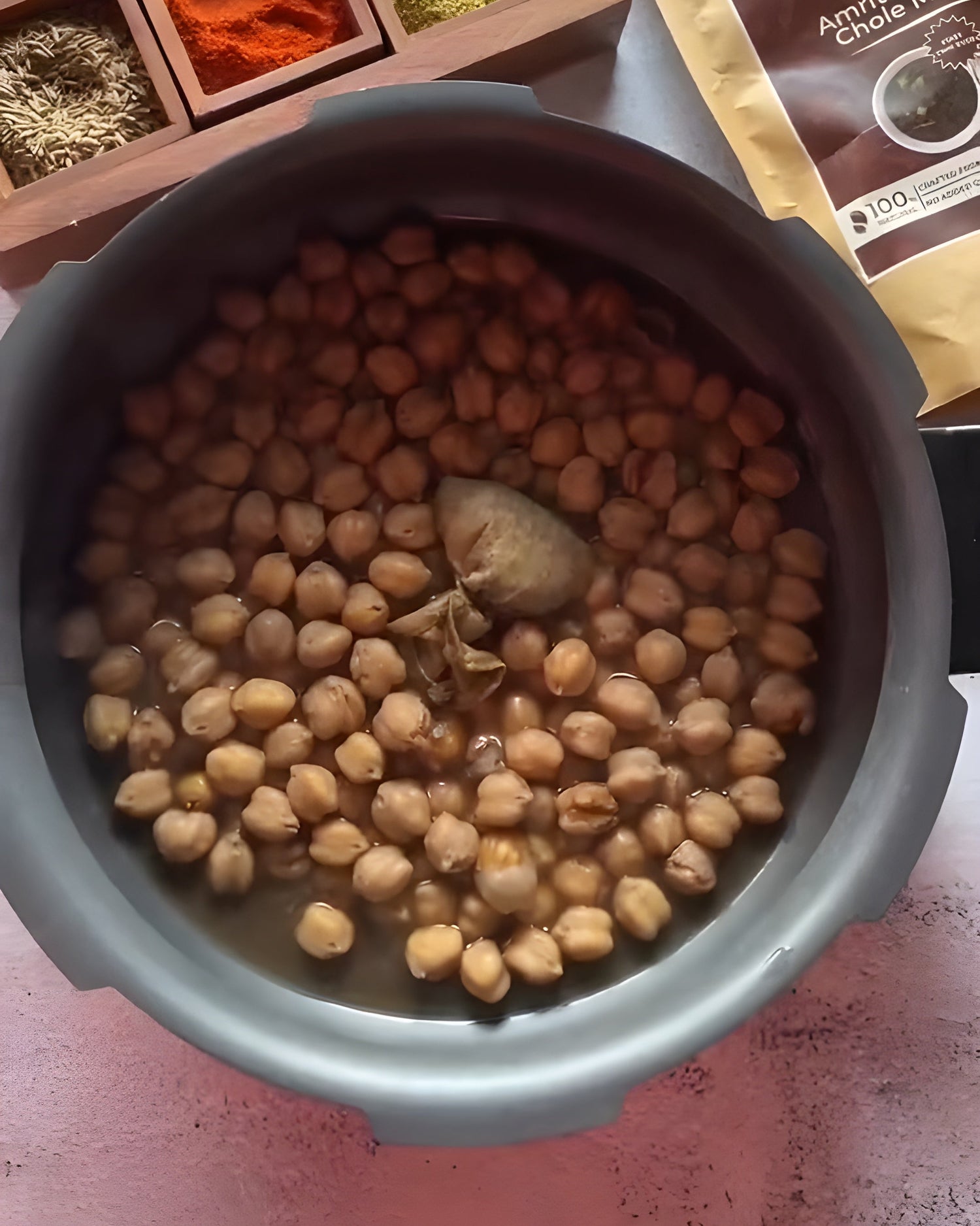 Cooked chickpeas in a pot with Heri-Infuse Potli & HeriMore spices and a package of Amritsari Pindi Chole Masala on a table.